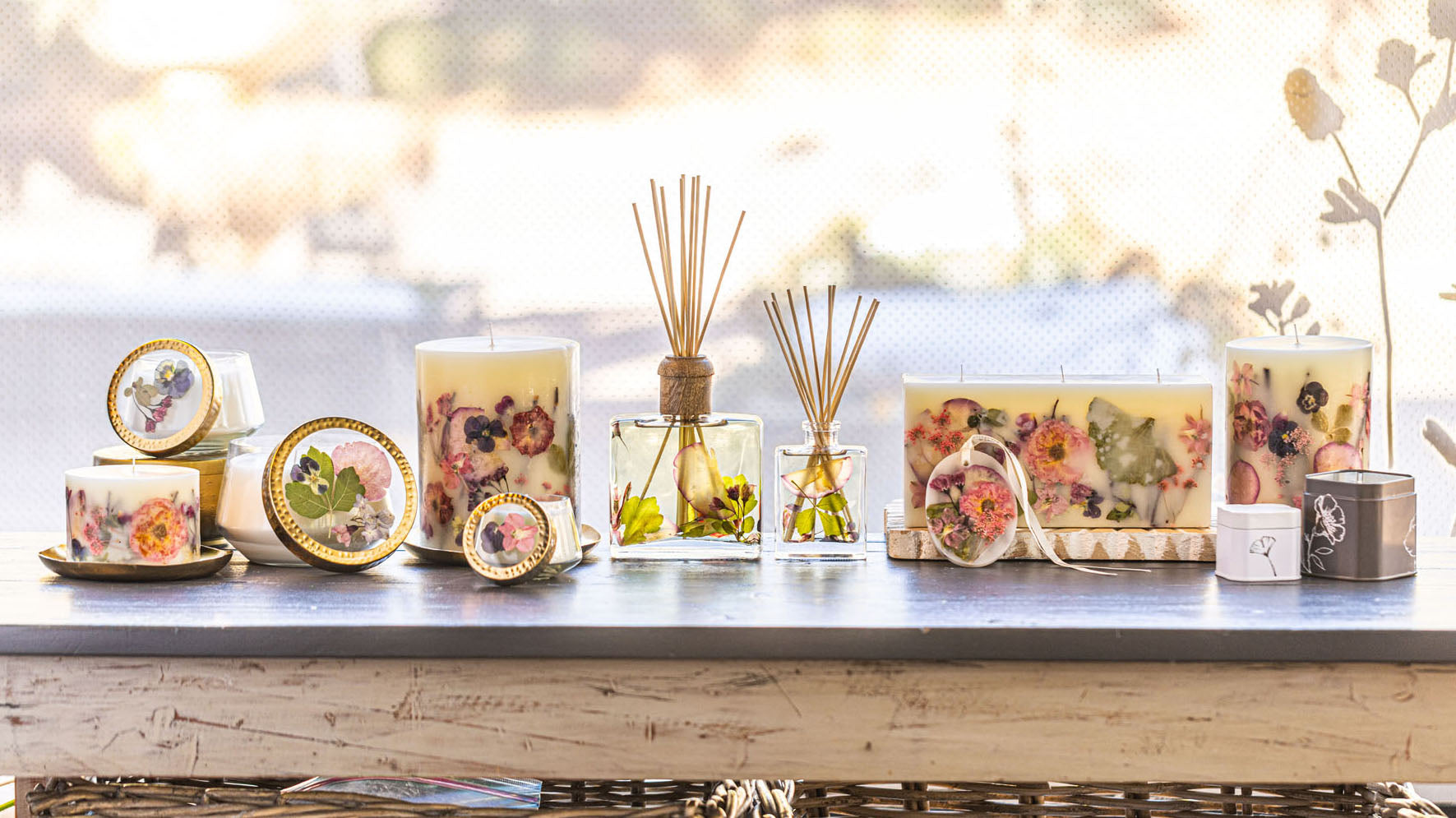 Decorative candles and floral diffusers on a rustic wooden table, lit by soft natural light.
