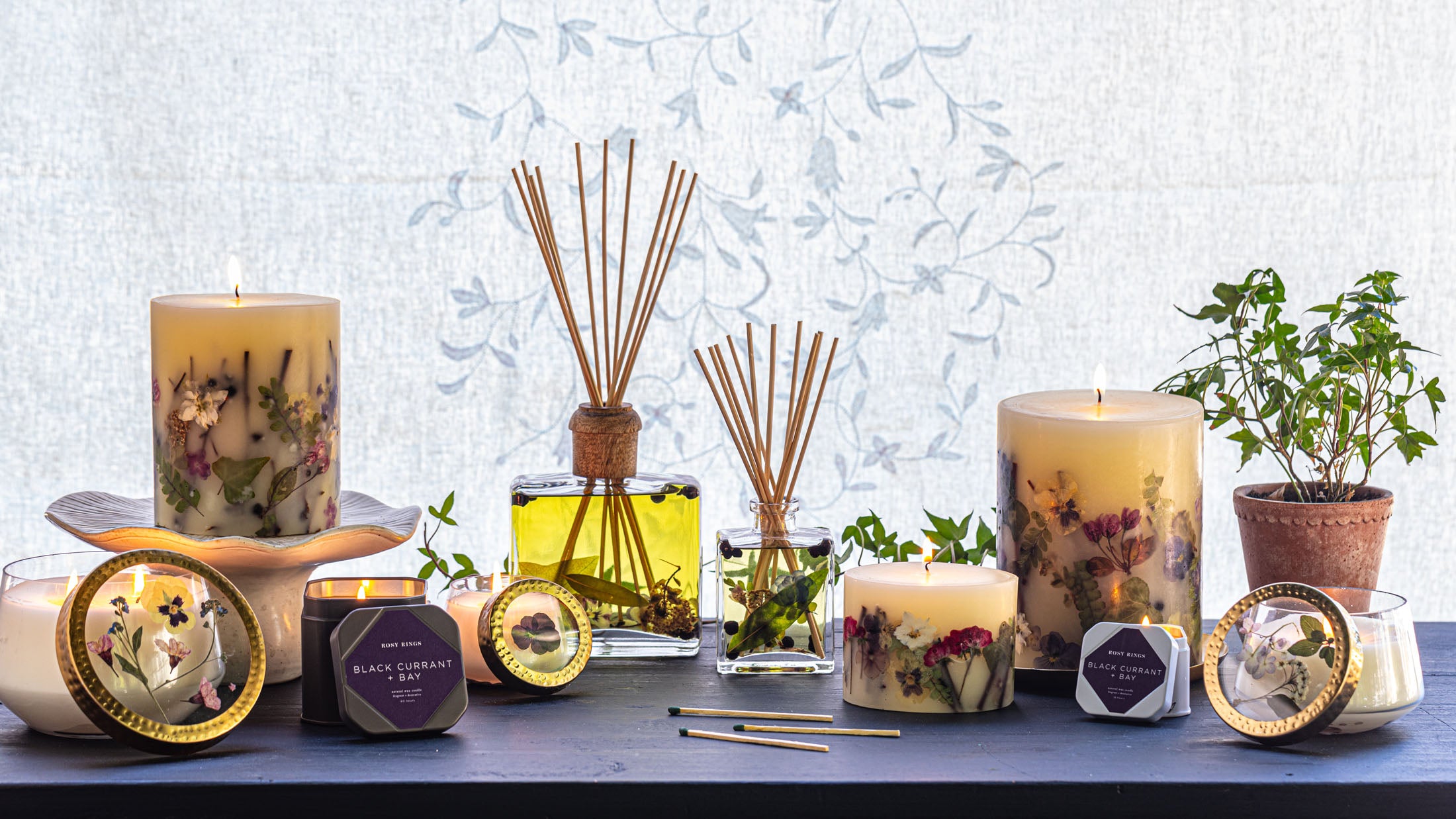 Fragrant candles and floral reed diffusers on a wooden table with a soft, patterned background.