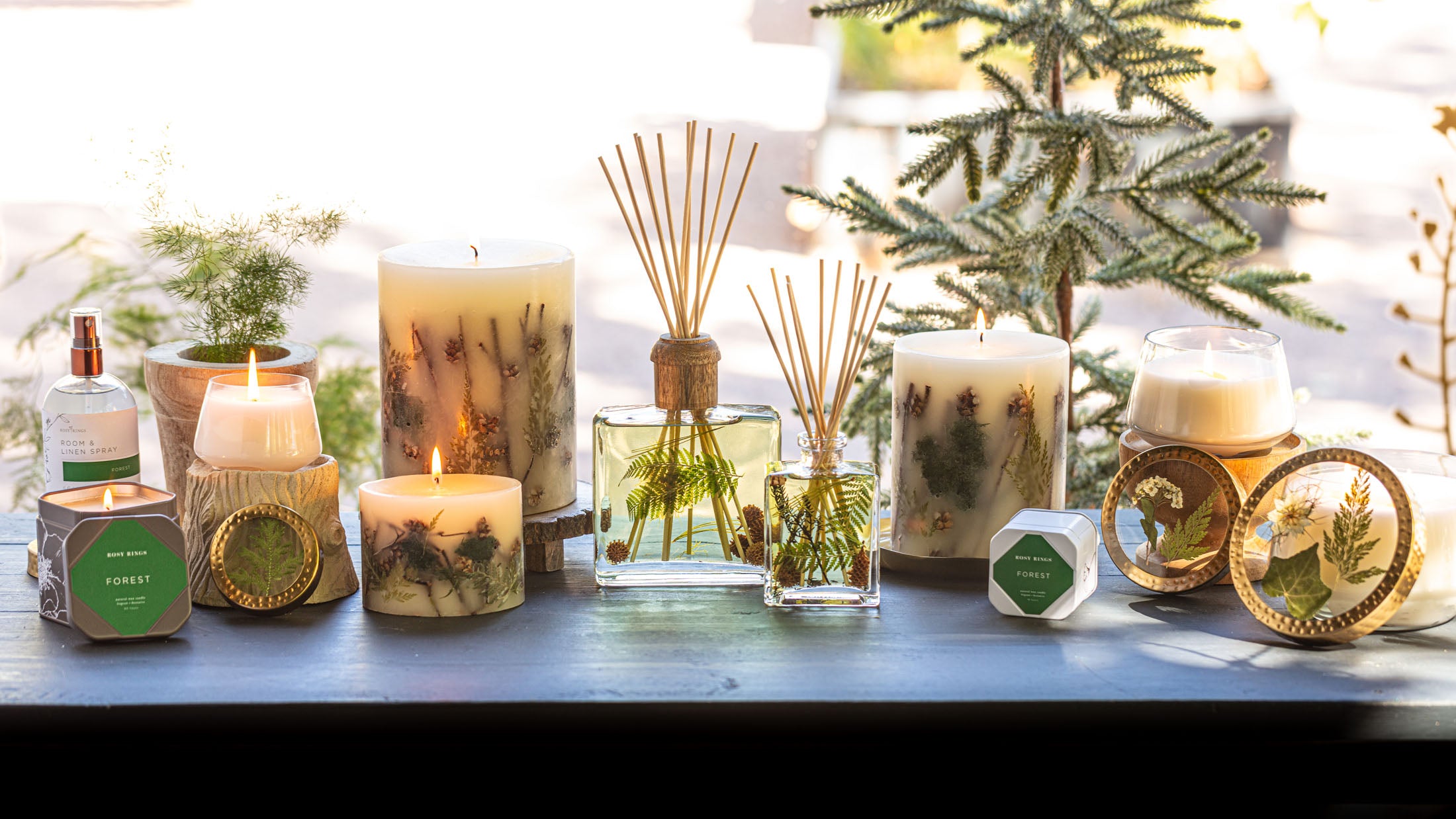 Decorative candles, room spray, and diffusers with natural elements displayed on a wooden table by the window.