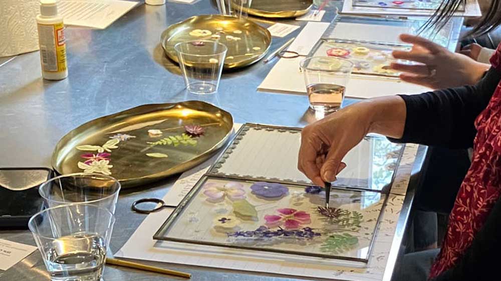 A woman carefully arranges colorful flowers in a vase, focusing intently on her floral design