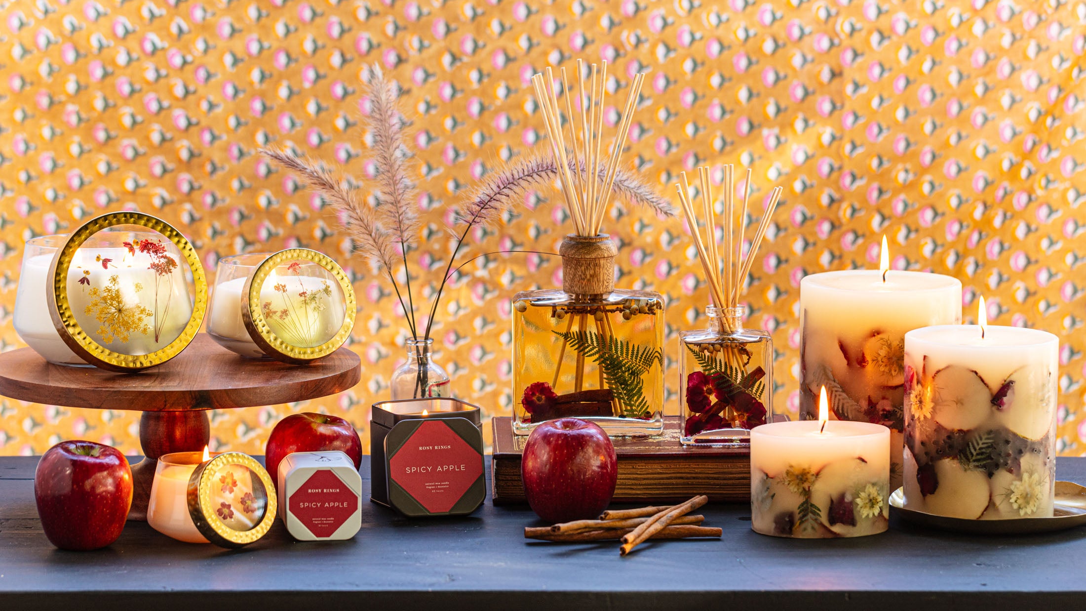 A cozy display of scented candles, essential oils, and fresh apples against a vibrant patterned backdrop.